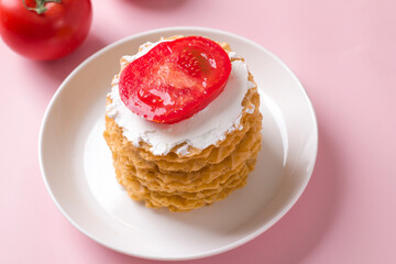 A stack of thin salty waffles with creamy sauce and tomato