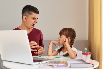 Indoor shot of angry aggressive father screaming at his daughter while helping her to do homework,...