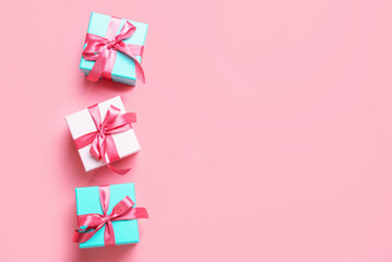 Three gift boxes with ribbons on pink background close-up, top view