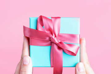 Female hands holding gift box with pink ribbon close-up top view.