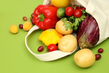 Cotton bag with vegetables and fruits on green background