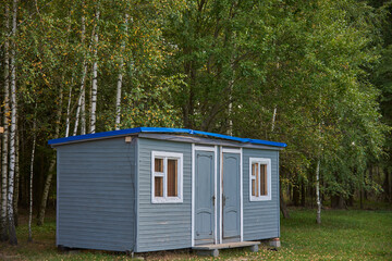 A small summer house stands in a clearing against the background of birch trees.