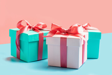Three gift boxes with ribbons on pink and blue background close-up, front view