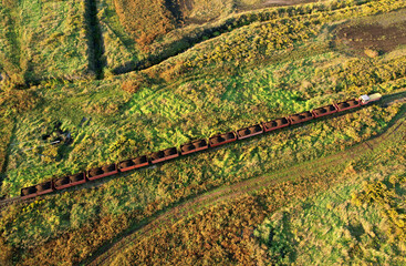 Train transports peat in freight wagons from peat extraction. Aerial view of the diesel locomotive on railroad in landscape at wetlands. Drone view of the peat bog railway at peatlands.