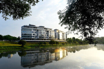 Obraz premium Modern residential building overlooking the river. Design of the facade of a multi-storey home with plastic windows and balconies. Elite penthouse overlooking the lake in the city park