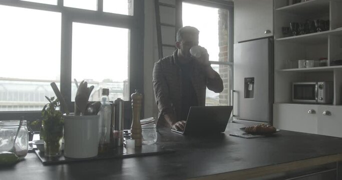 Mid adult hispanic male using laptop in kitchen