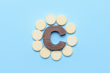 Letter C and vitamin pills on color background