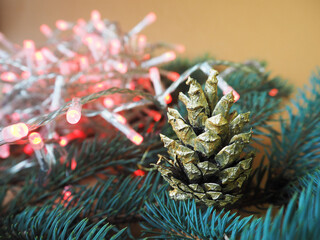 a cone painted in gold color lies on the branches of a blue Christmas tree next to a red glowing garland . side view