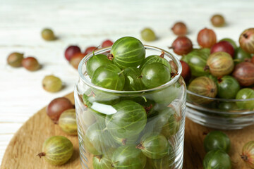Board with jar and bowl of gooseberry on white wooden background
