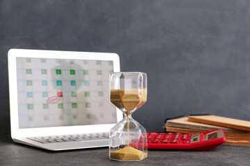Hourglass and laptop on dark background