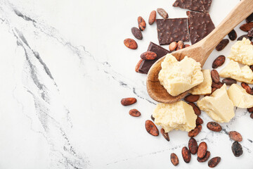 Spoon with cocoa butter, beans and chocolate on light background