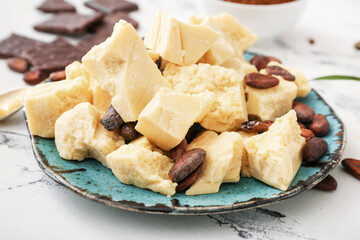 Plate with cocoa butter and beans on light background