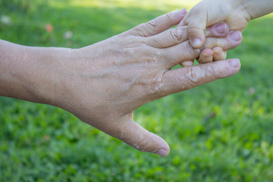 A close-up photo with a child's hand that is pulling his grandma's hand to go to play together. grandma's hand have spots, that looks like vitiligo disease.