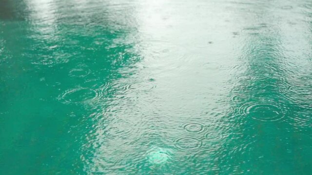 slow-motion of water pool with rain falling drops on the surface