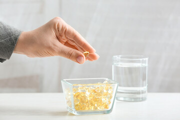 Woman taking fish oil pill from bowl on table, closeup
