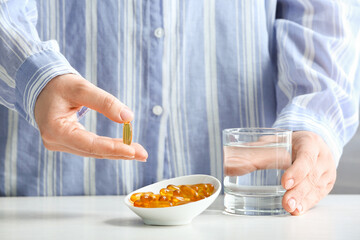 Woman taking fish oil pill from bowl on table, closeup
