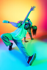 Close-up two hip-hop dancers, stylish emotive girl and boy in action and motion in casual sports youth clothes on gradient multi colored background at dance hall in neon light.