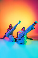 Young people, hip-hop dancers, stylish emotive girl and boy in action and motion in casual sports youth clothes on gradient multi colored background at dance hall in neon light.