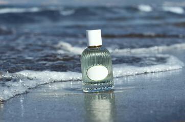 Blue perfume bottle stands on wet sand on the background of waves and the sea, perfume mock up on...