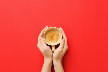Female hand with cup of coffee on red background