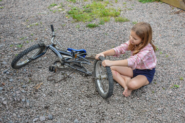 Fototapeta na wymiar the child girl has damaged a bicycle wheel and is making repairs photo without processing