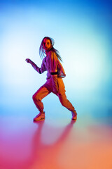 Portrait of young sportive girl dancing hip-hop in stylish clothes on colorful background at dance hall in neon light. Youth culture, movement, style and fashion, action.