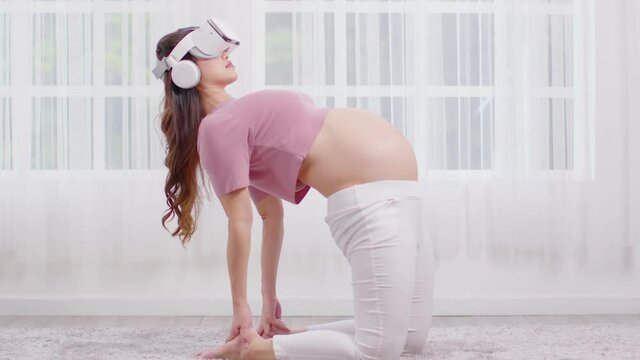 Happy Asian Pregnant Woman Using Virtual Reality Glasses For Practice Yoga Online Class Ustrasana Pose Or Yoga Camel Pose To Meditation Smile With Big Belly Relax At Home.Pregnancy Technology Concept