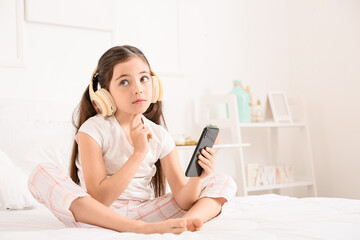 Little girl with headphones and mobile phone listening to audiobook in bedroom