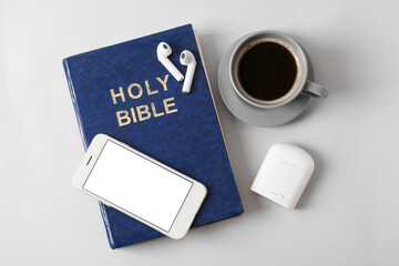 Holy Bible, earphones, cup of coffee and mobile phone on light background