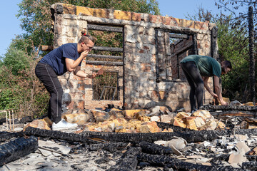 Young couple grub out of the ruins of house destroyed with fire. Damaged window, walls and floor,...