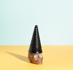 Brown skull with witch hat made of black ice cream cone. Minimal spooky concept. Halloween or Santa Muerte background. Creative and funny holiday idea.