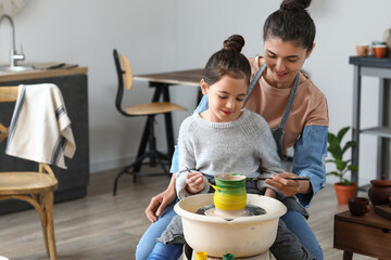 Little girl with her mother painting ceramic pot at home