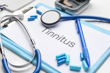 Clipboard with word TINNITUS, stethoscope and pills on white background