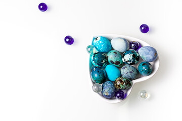 Easter blue quail eggs in a plate in the shape of a heart on a white table