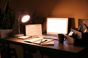 Modern workplace with computer and glowing lamp near color wall