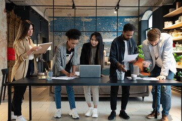 Group of young multiracial people in casual discussing strategy plan of collaboration standing at table in modern office