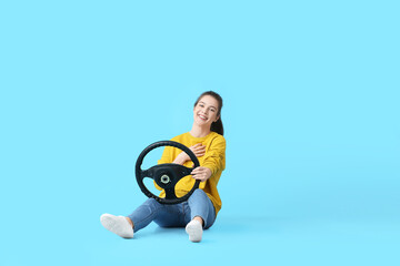 Young woman with steering wheel on color background