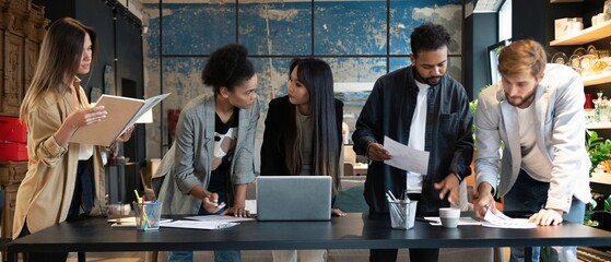 Group of young multiracial people in casual discussing strategy plan of collaboration standing at table in modern office