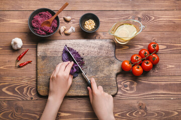 Woman preparing tasty pesto sauce on wooden background