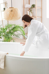 Young woman running bathtub with warm water at home