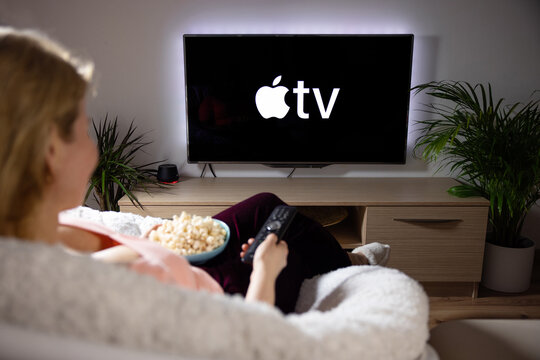 Riga, Latvia - April 14, 2021: Woman watching television at home, Apple TV logo on the screen.