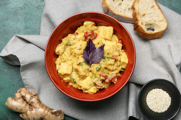 Bowl of tasty chicken curry and ingredients on color background