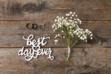 Wedding and engagement rings, gypsophila flowers, text BEST DAY EVER on wooden background