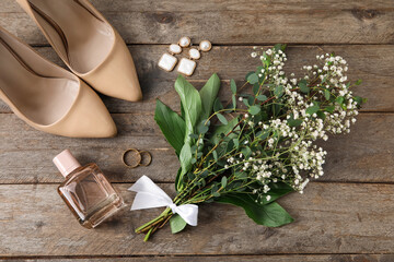 Wedding rings, bride accessories and bouquet of flowers on wooden background