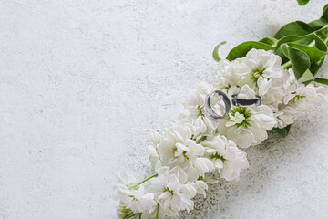 Pair of wedding rings and beautiful flowers on light background