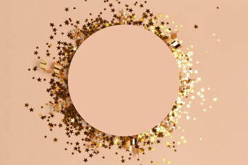 Round frame made of gold colored confetti on a beige background.