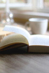 Bowl of cookies, cup of hot beverage, open book and lit candles on a table. Selective focus.