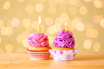 Tasty Birthday cupcakes with burning candles on table against blurred lights