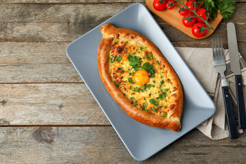 Plate with tasty Ajarian khachapuri on wooden background