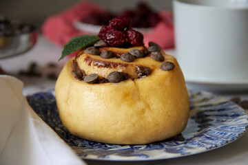 cinnamon roll in blue earthenware plate with chocolate chips and blueberries on white tablecloth